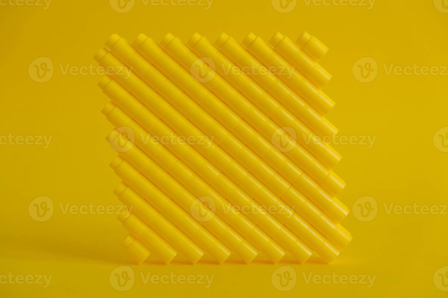 Yellow plastic building blocks in shape of a cube on yellow background photo