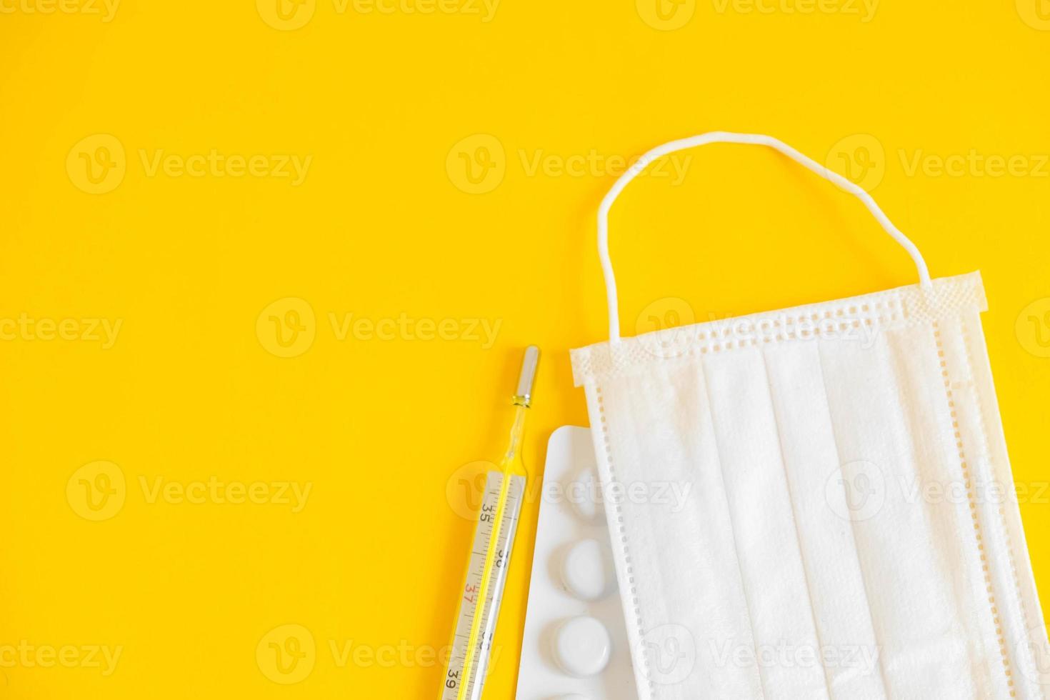 Medical disposable mask, pills and a mercury thermometer on a yellow background photo