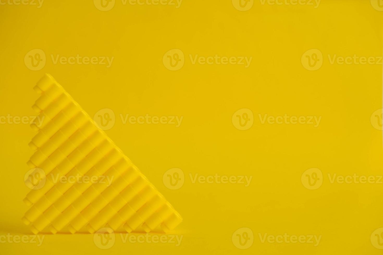 Yellow plastic building blocks in the shape of a pyramid on yellow background photo