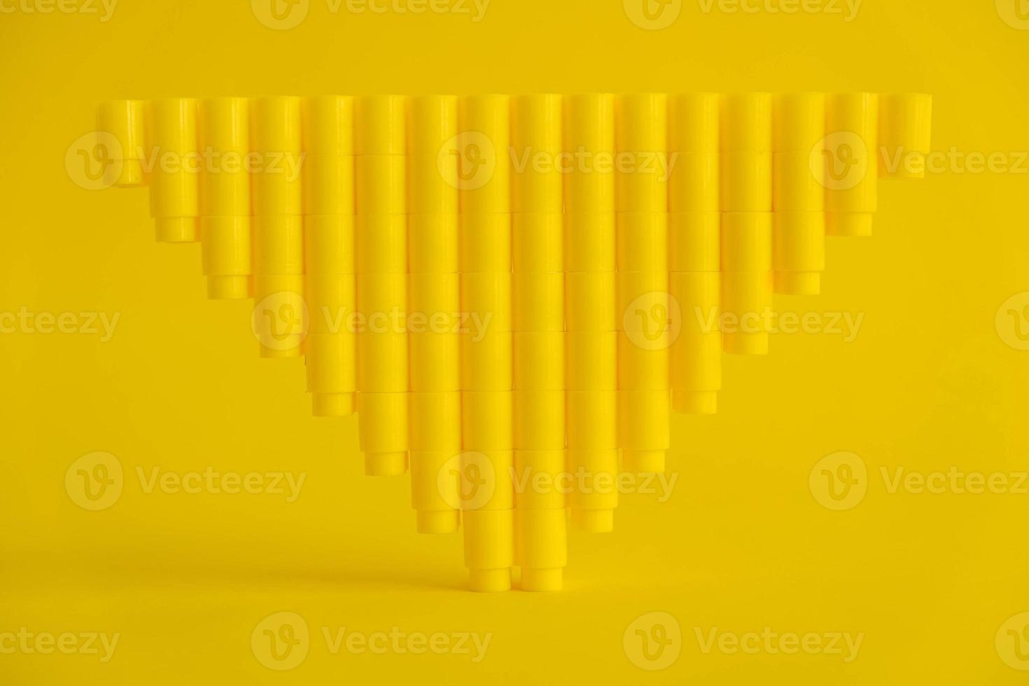 Yellow plastic building blocks in shape of a pyramid on yellow background photo