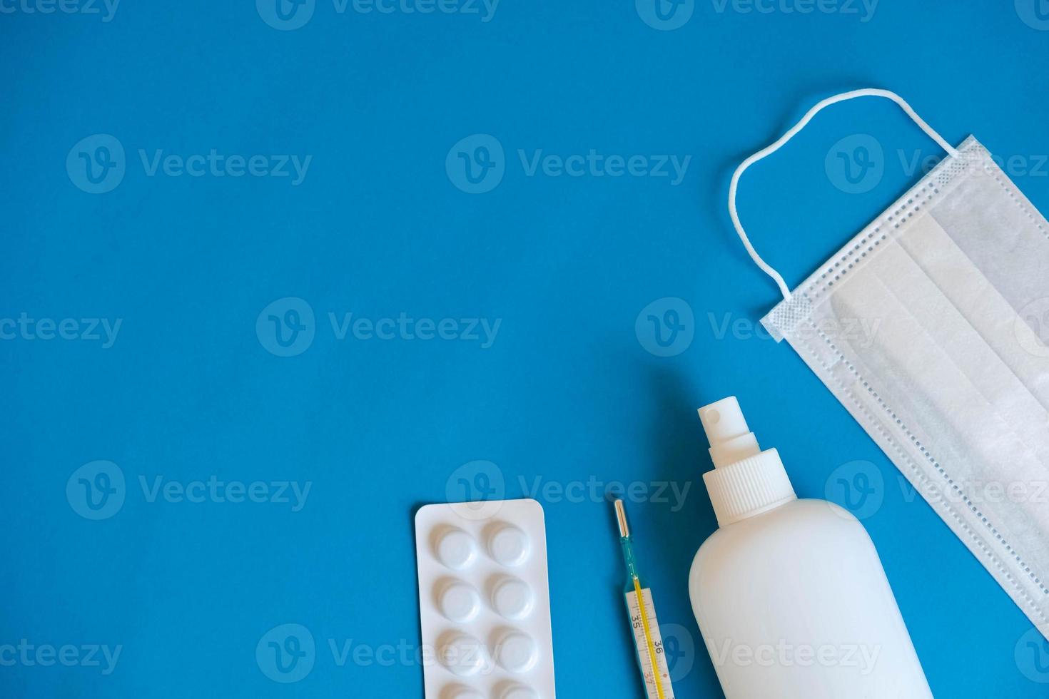 Set of medical disposable mask, antiseptic, pills and a mercury thermometer on a blue background. Medical hygiene and virus protection concept. Top view. Copy, empty space for text photo