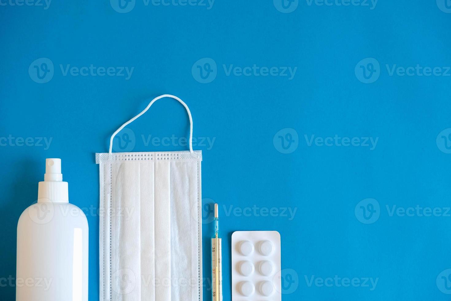A set of medical disposable mask, antiseptic, pills and a mercury thermometer on a blue background. Medical hygiene and virus protection concept photo