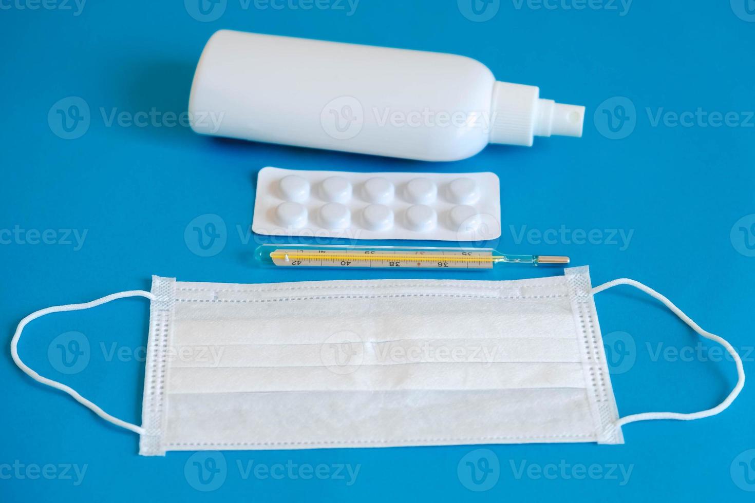 un conjunto de mascarilla médica desechable, antiséptico, pastillas y un termómetro de mercurio sobre un fondo azul. concepto de higiene médica y protección antivirus foto