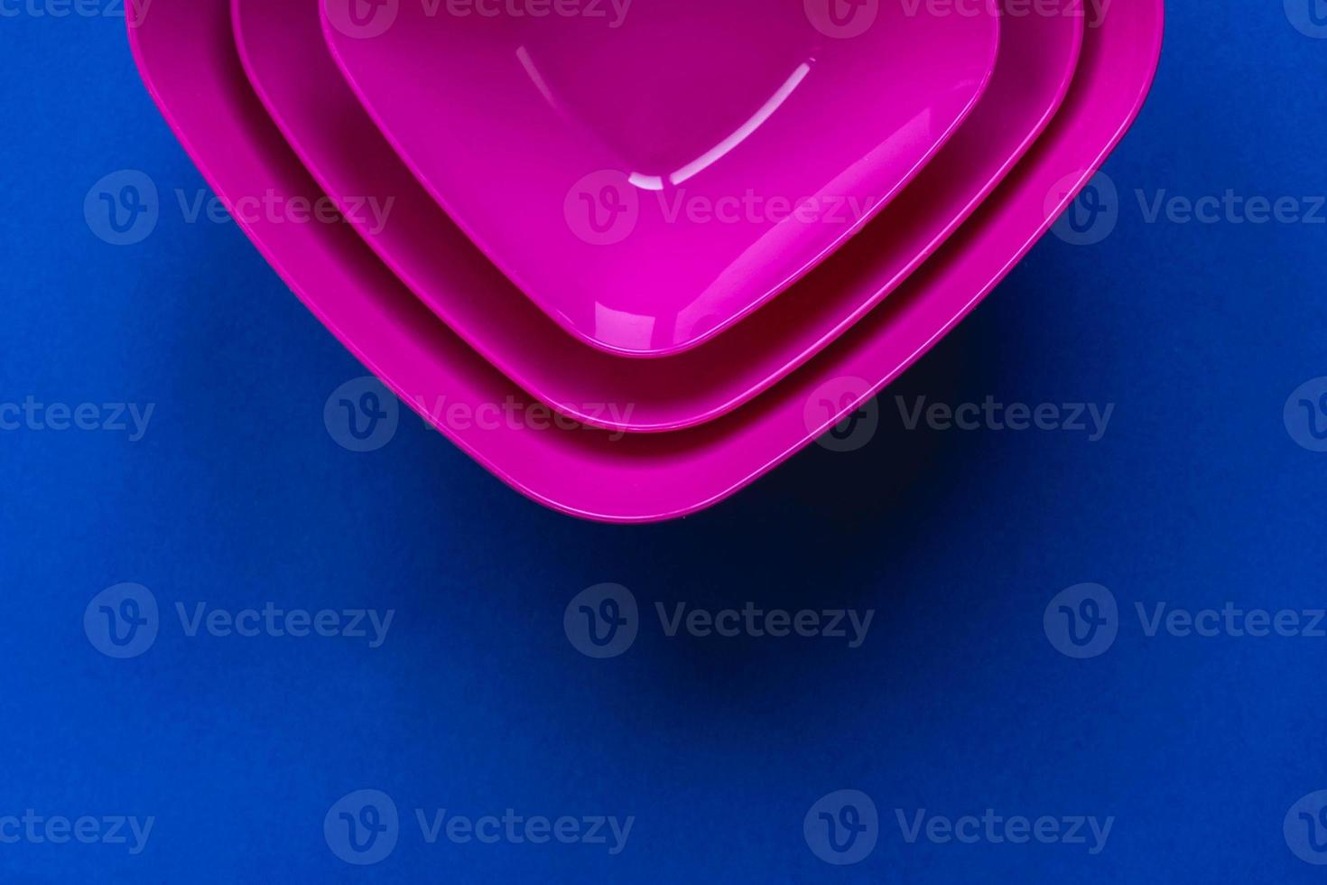 Set of pink plates on blue background. Plastic utensils for the kitchen photo