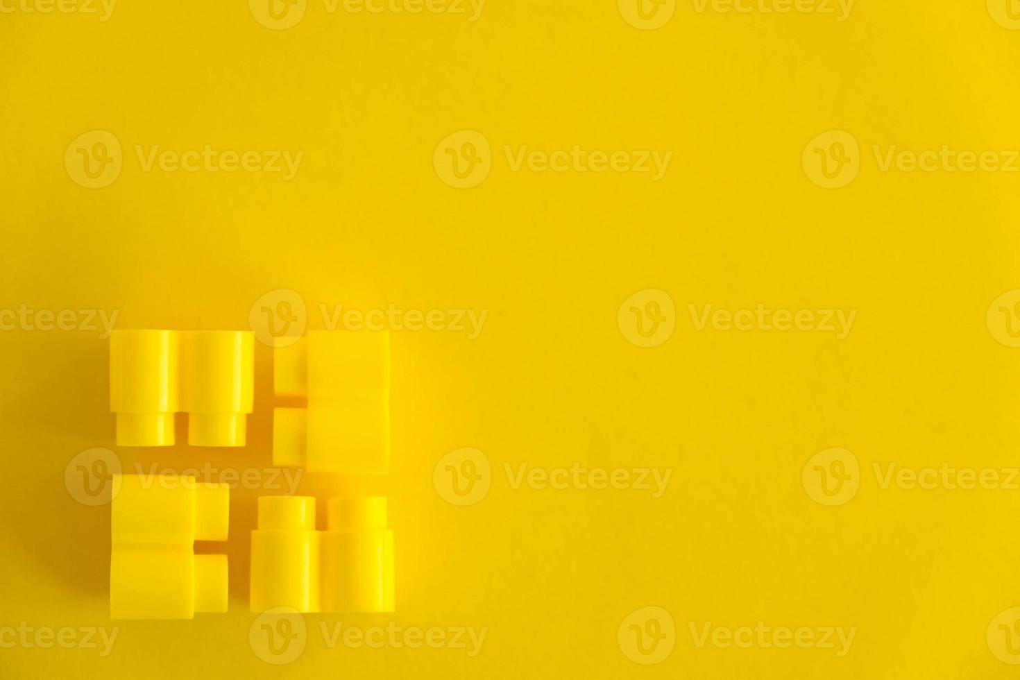 Yellow plastic building blocks on yellow background. Background of plastic details building blocks photo