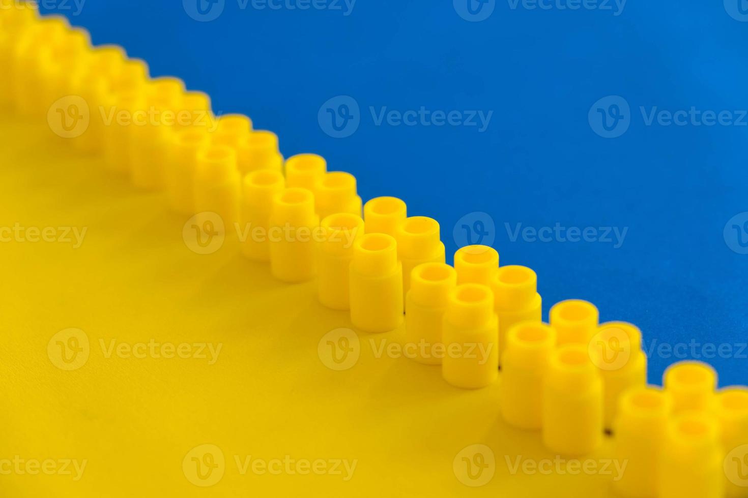 Yellow plastic building blocks on blue and yellow background. Pieces and elements of constructor. Parts of bright small spare parts for toys. Top view. Copy, empty space for text photo