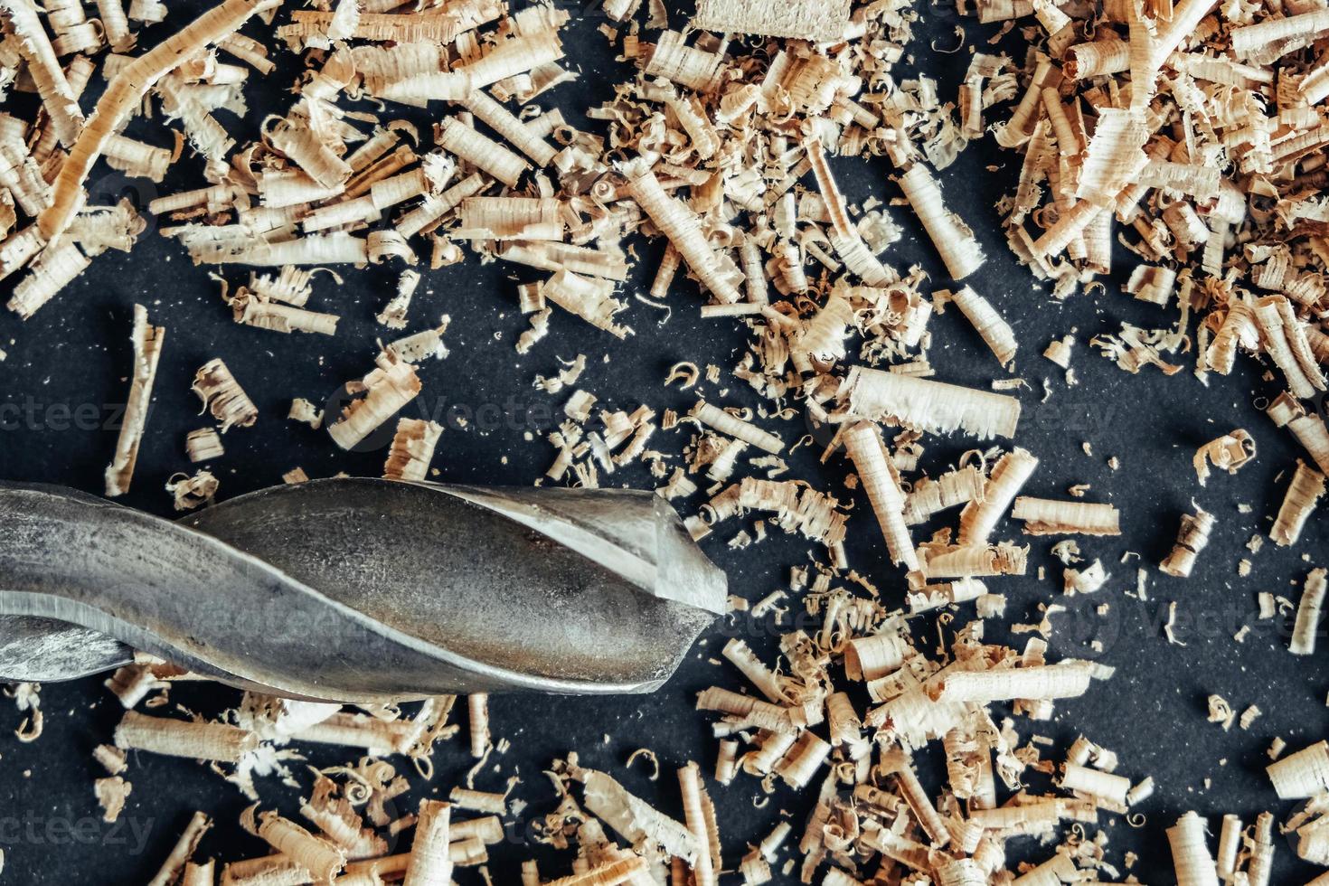 Wood drill bit with wooden shavings on black background photo