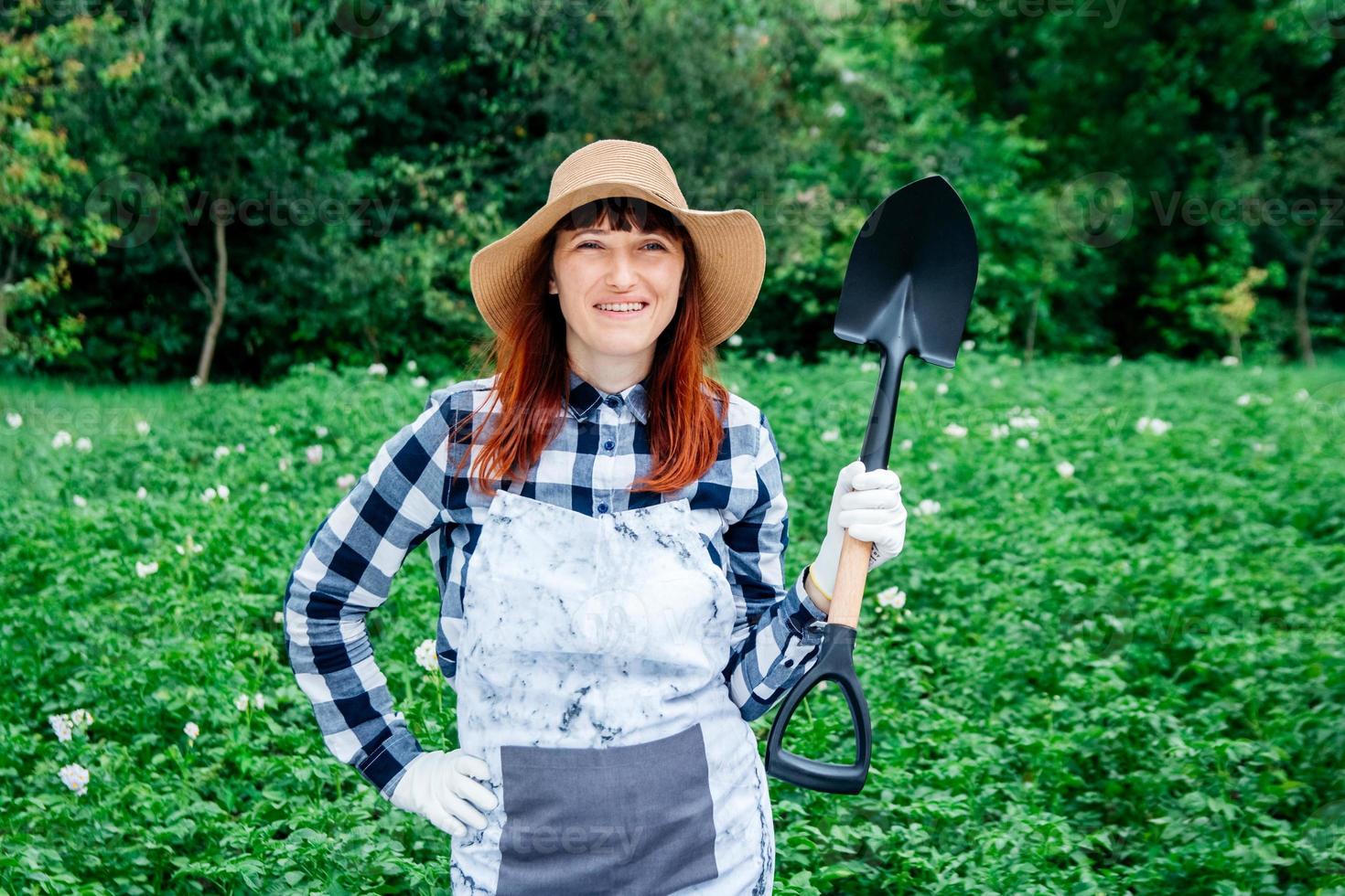 La agricultora con una pala con un sombrero de paja en el fondo de un huerto foto