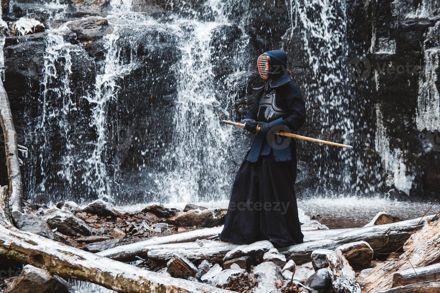 Man practicing kendo with bamboo sword on waterfall, rocks and forest background photo