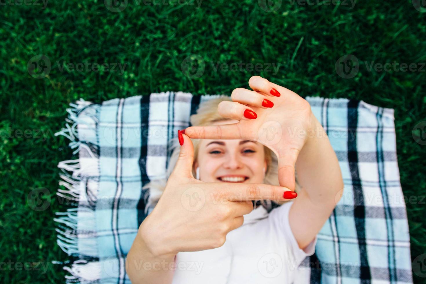 Mujer sonriente haciendo bastidor con las manos y los dedos con cara feliz acostado sobre una alfombra fondo verde foto