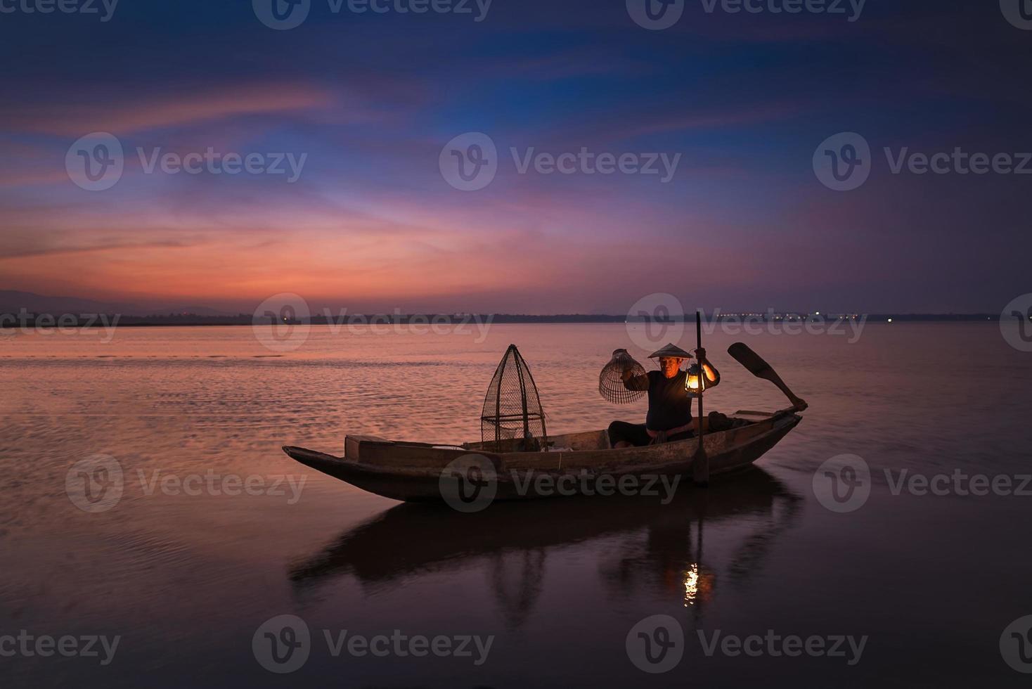 Asian fisherman with his wooden boat in nature river at the early morning before sunrise photo