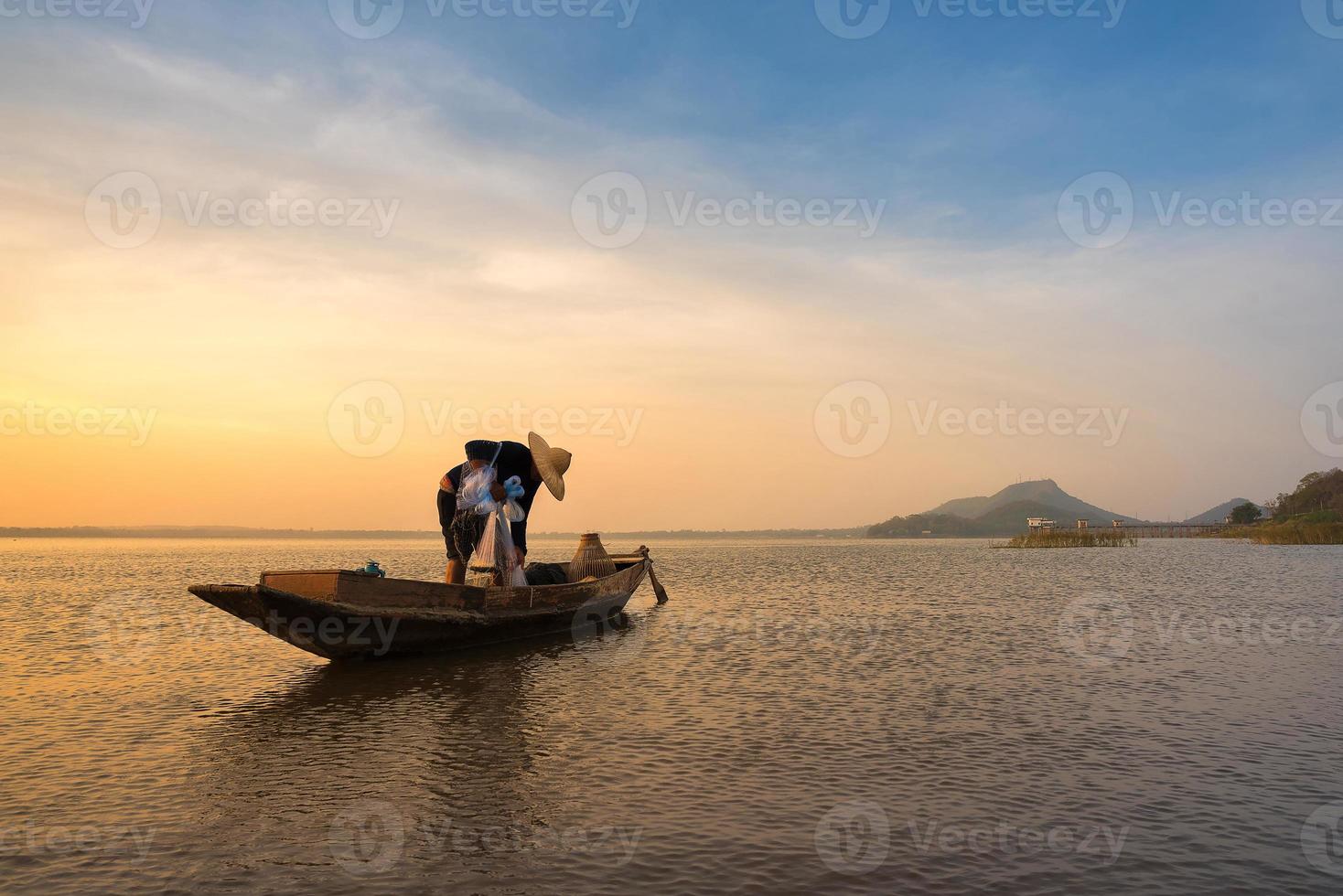 Asian fisherman on wooden boat preparing a net for catching freshwater fish in nature river in the early morning before sunrise photo
