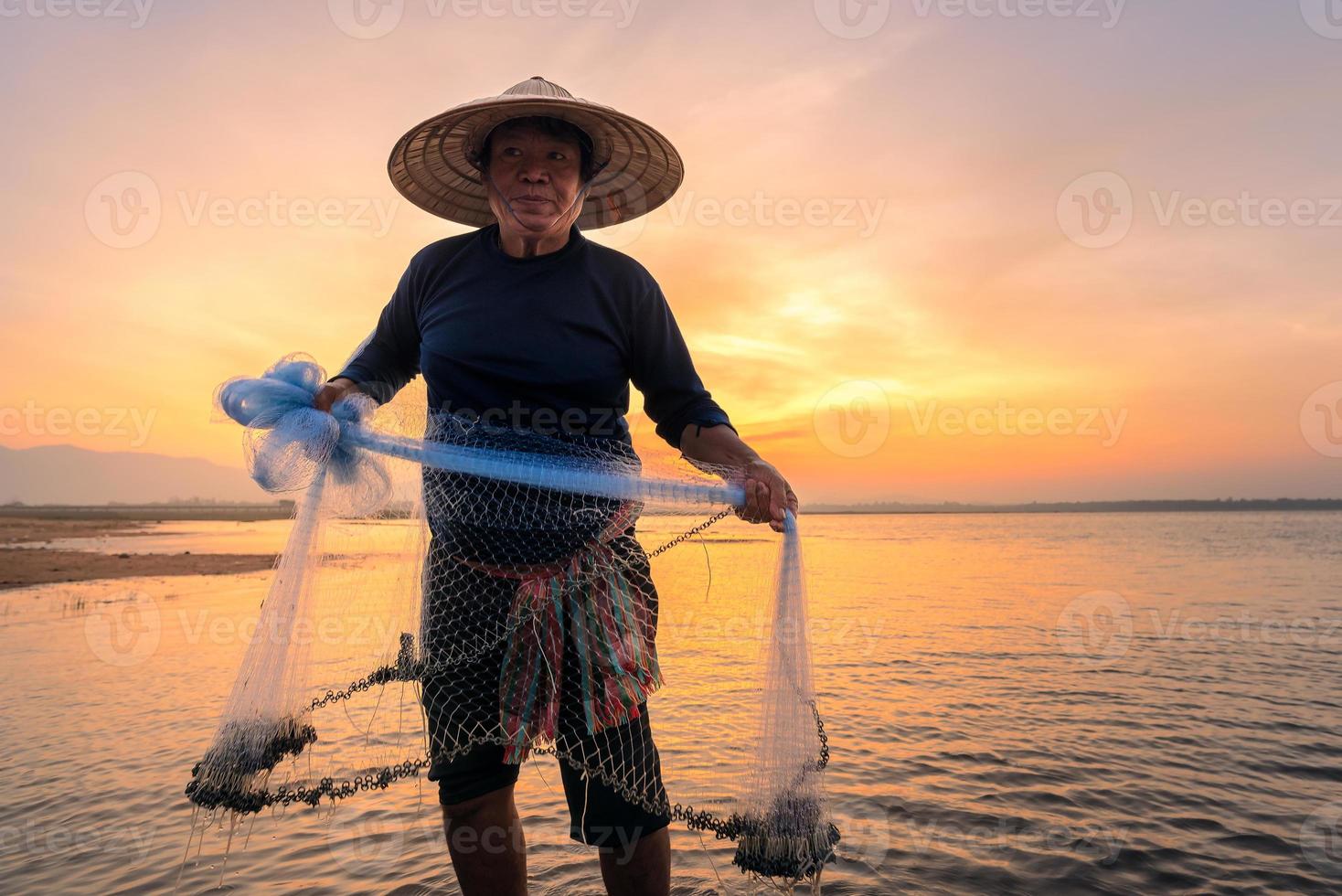 Silueta de pescador asiático sostenga una red para pescar peces de agua dulce en el río natural temprano en la mañana antes del amanecer foto