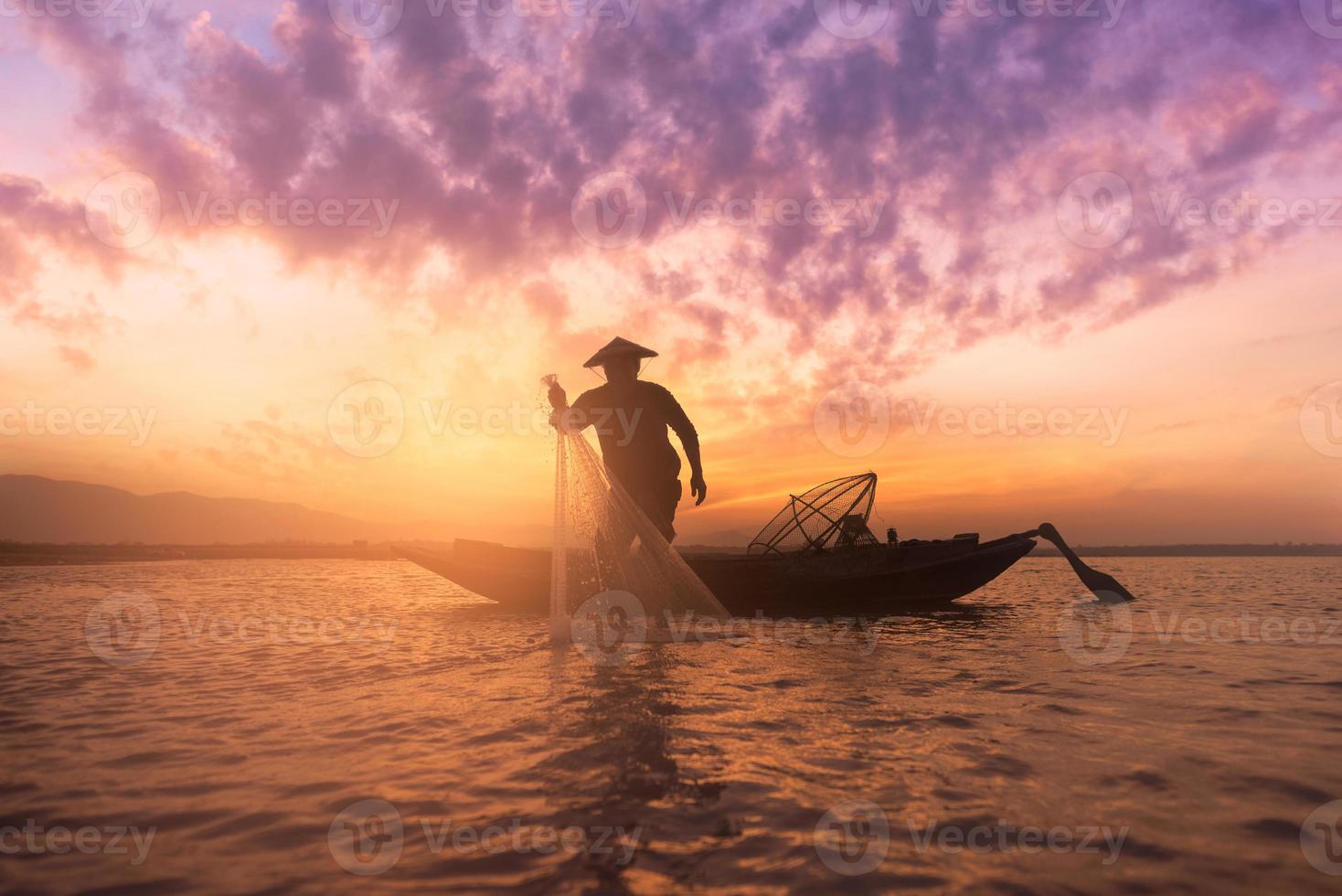 Silhouette asian fisherman holding a net for catching freshwater fish in nature lake during sunrise photo