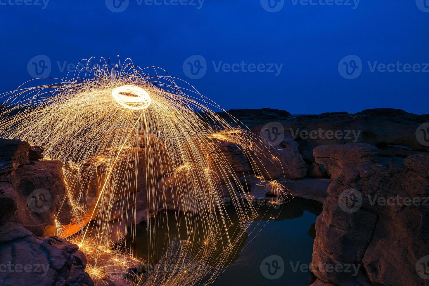 Long exposure capture of Burning steel wool being spun before dusk on a grand canyon rock field of Thailand photo