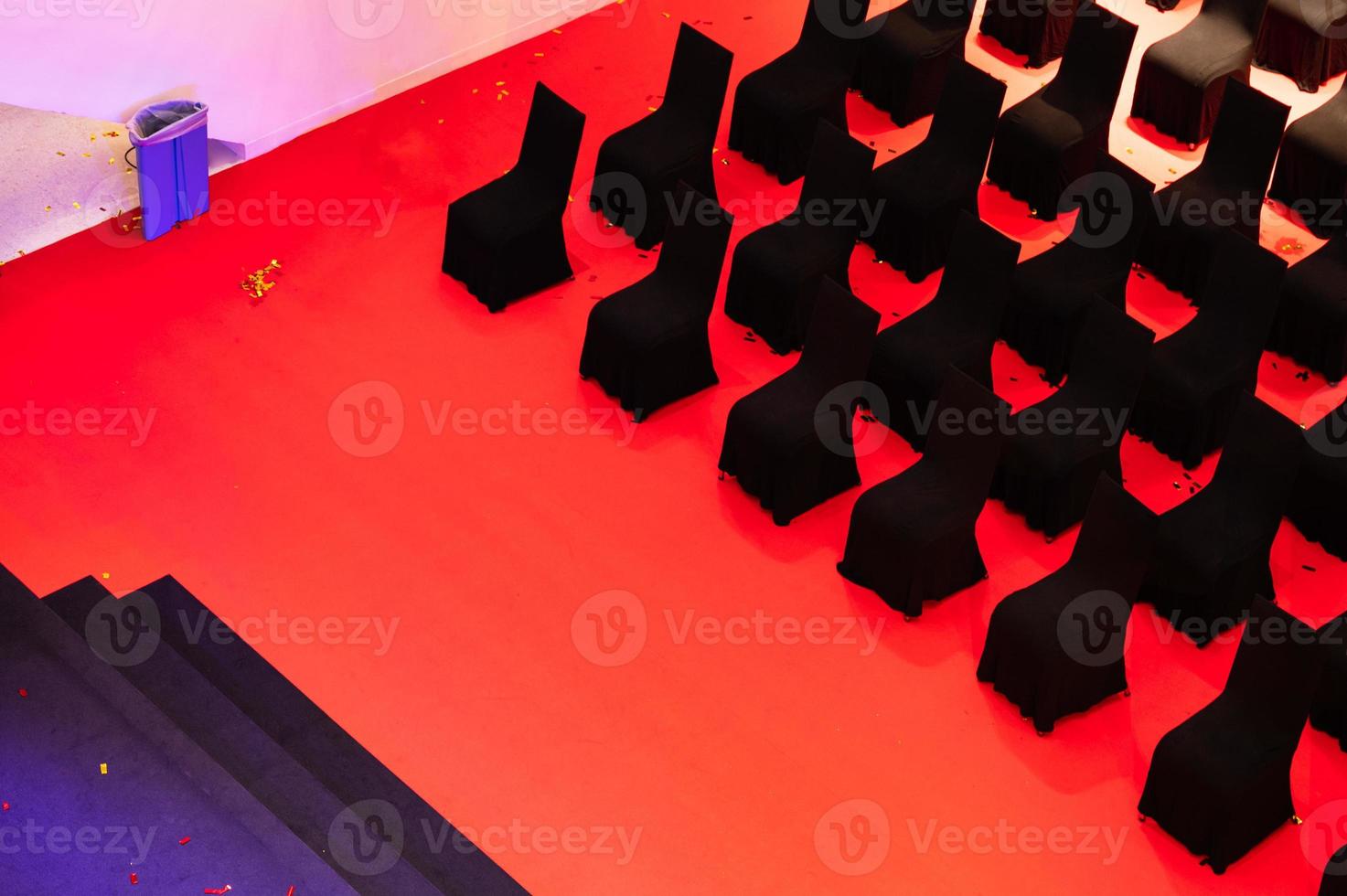 Row of empty black chairs on red floor in performance stage photo