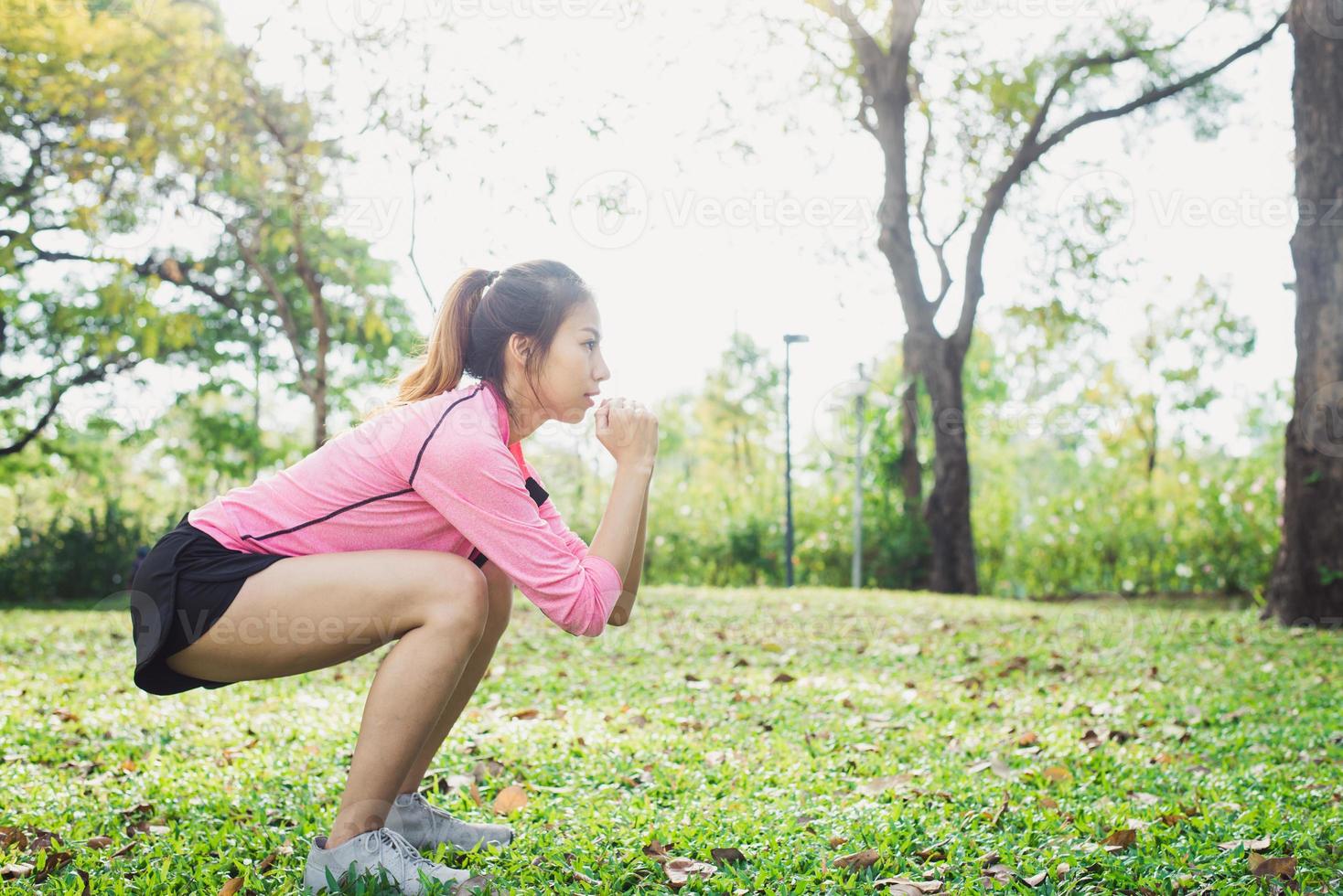 Young asian woman do squats for exercise to build up her beauty body in park environ with green trees and warm sunlight in the afternoon. Young woman workout exercise at the park. Outdoor exercising. photo