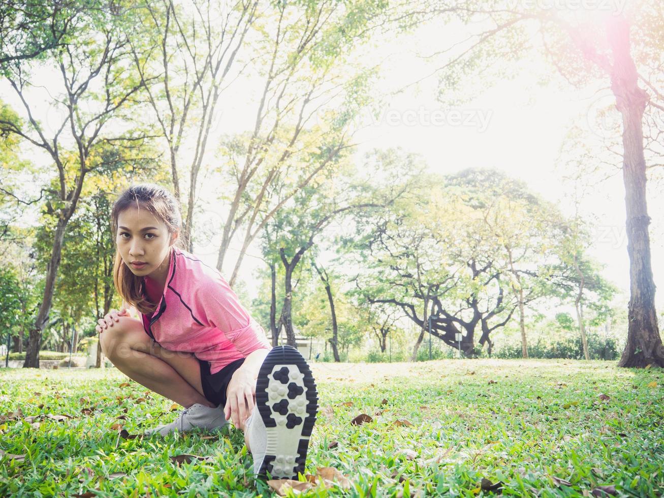 mujer asiática joven sana que ejercita en el parque. Colocar joven haciendo entrenamiento de entrenamiento en la mañana. joven mujer asiática feliz que se extiende en el parque después de un entrenamiento corriente. ejercicio concepto al aire libre. foto