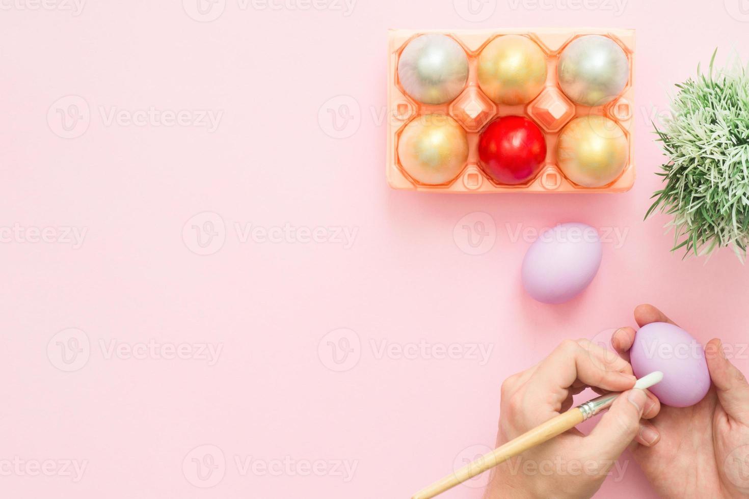 Top view person painting colorful easter egg painted in pastel colors composition with paint brush on pink pastel color background. Easter day background top view with copy space. photo