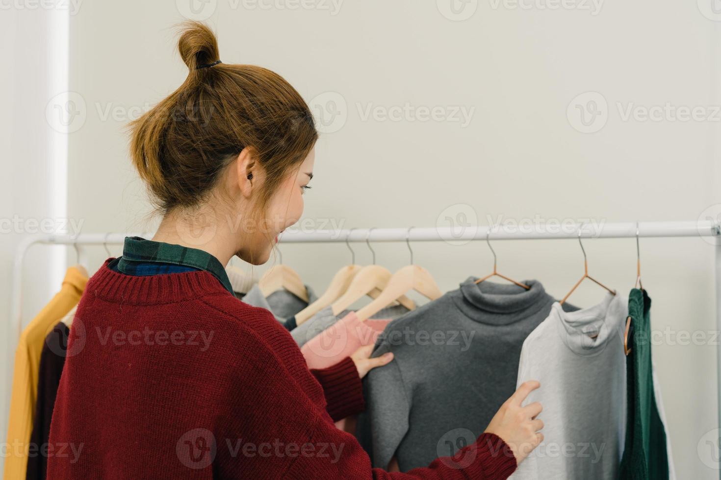 diseñadora de moda asiática trabajando, comprobando y eligiendo el diseño de ropa en el perchero mientras trabaja en el estudio de moda. estilo de vida hermosa mujer diseñador profesional concepto de trabajo. foto