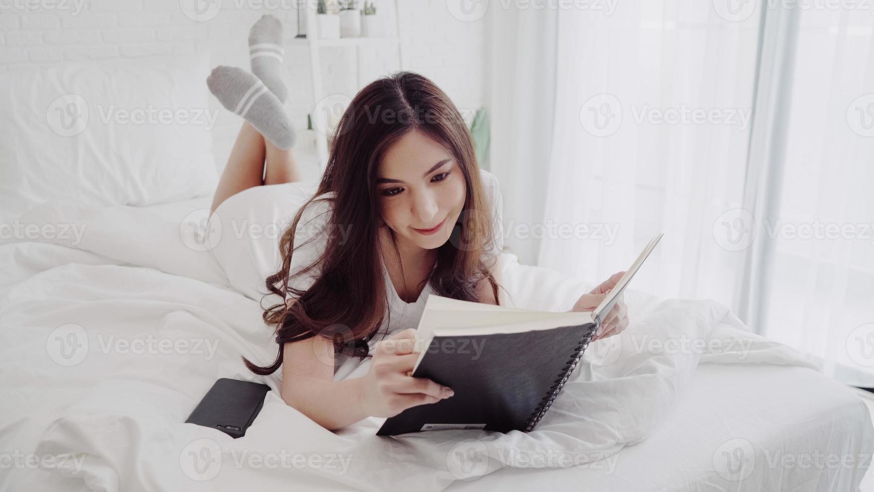 Portrait of beautiful attractive Asian woman reading a book while lying on the bed when relax in her bedroom at home. Lifestyle women using relax time at home concept. photo