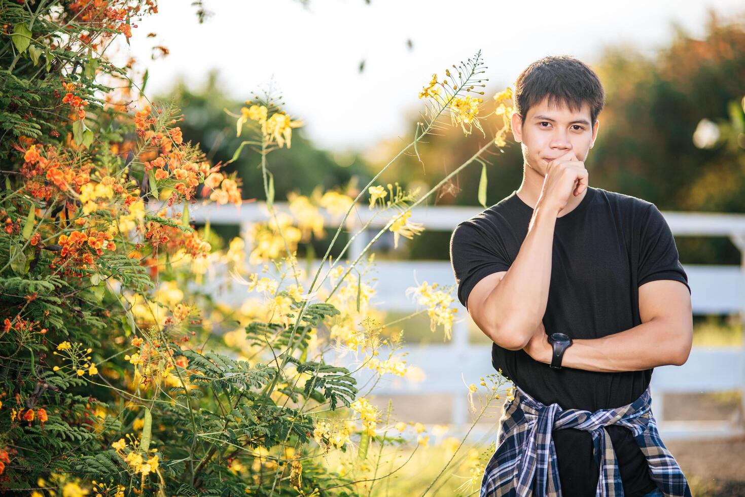 The male traveler wears a black shirt and stands in a flower garden. photo