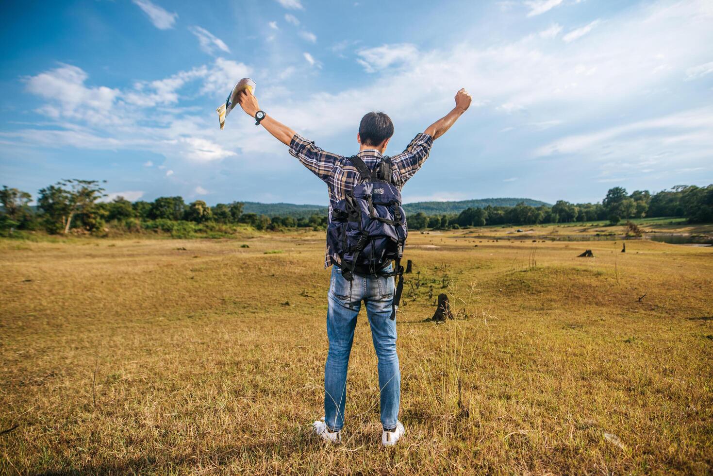 un viajero masculino con una mochila que lleva un mapa y de pie en el prado. foto