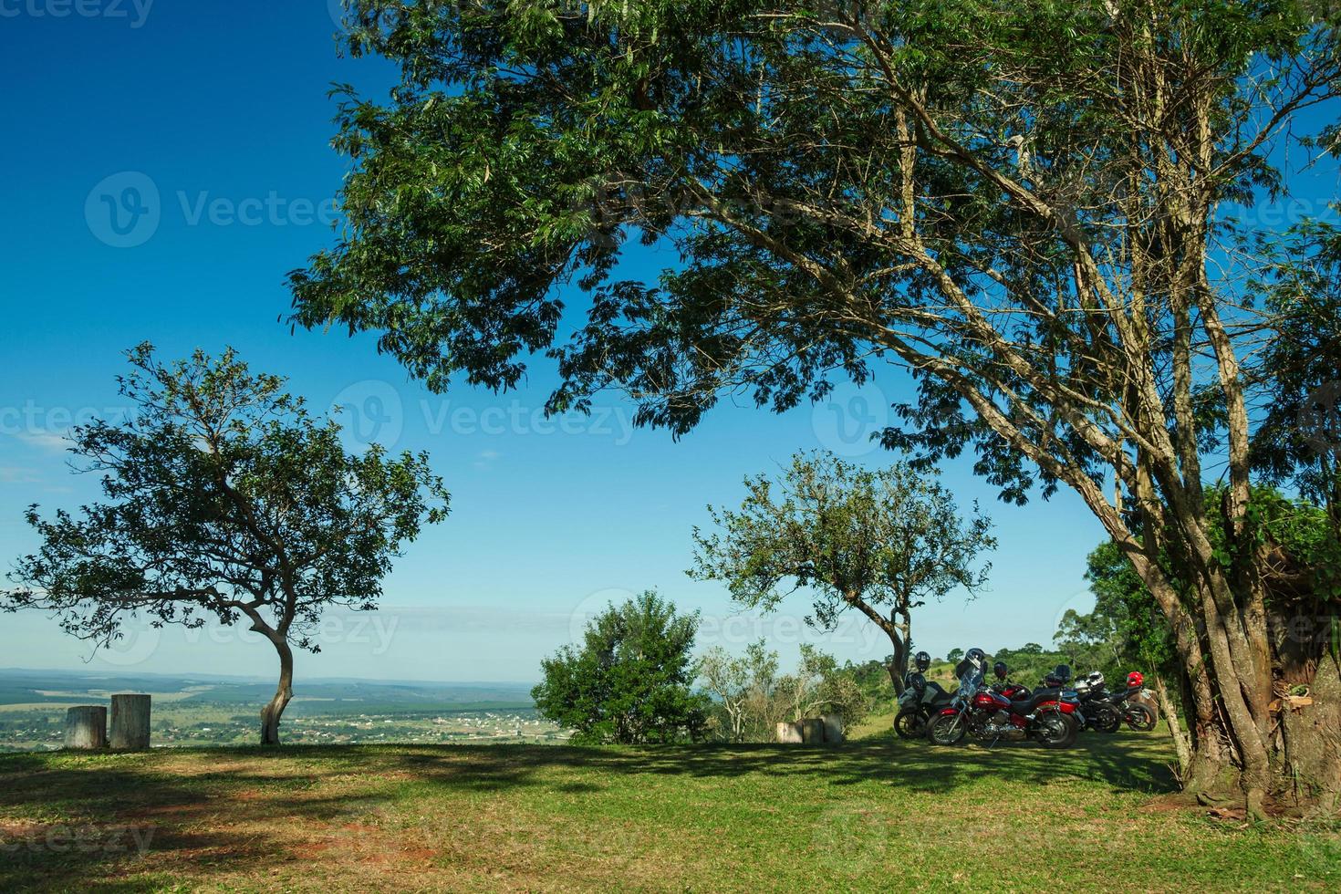 Varias motocicletas estacionadas bajo la sombra de los árboles, en la cima de una colina cubierta por un prado verde y un día soleado cerca de pardinho. un pequeño pueblo rural en el campo del estado de sao paulo. foto