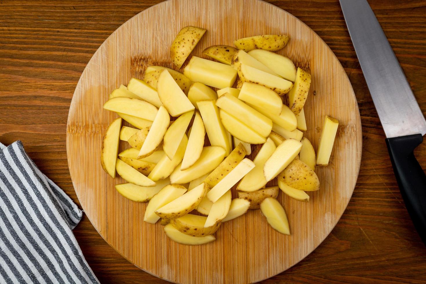 patatas crudas cortadas en patatas fritas sobre una tabla de madera. vista superior. foto