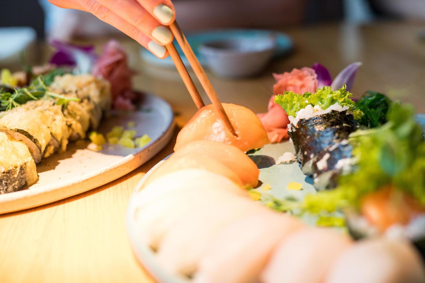 A person eating sushi at a restaurant. Visible chopsticks reaching for sushi. photo