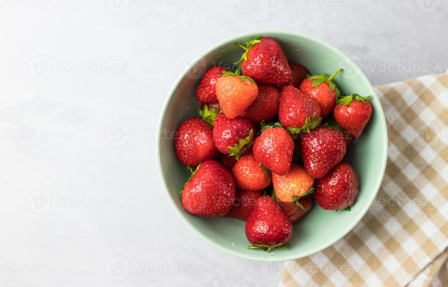 Fresh strawberries in a mint bowl on a white table from above photo