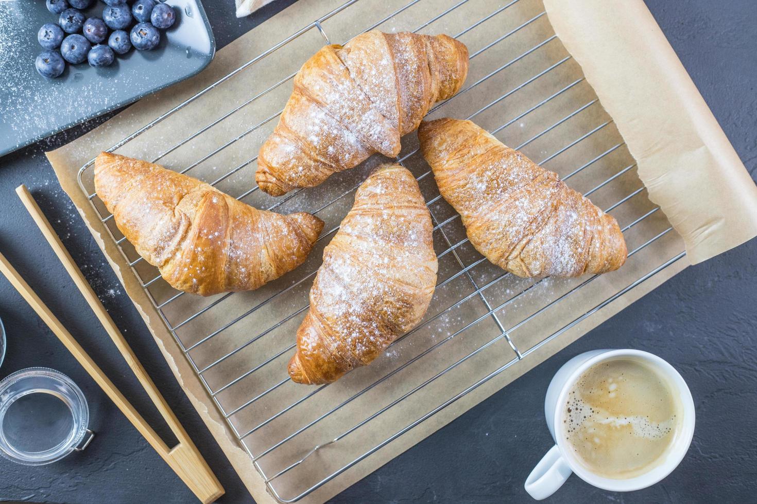 croissants acostado sobre una tabla de madera. fruta y café en los alrededores. desayuno francés. foto