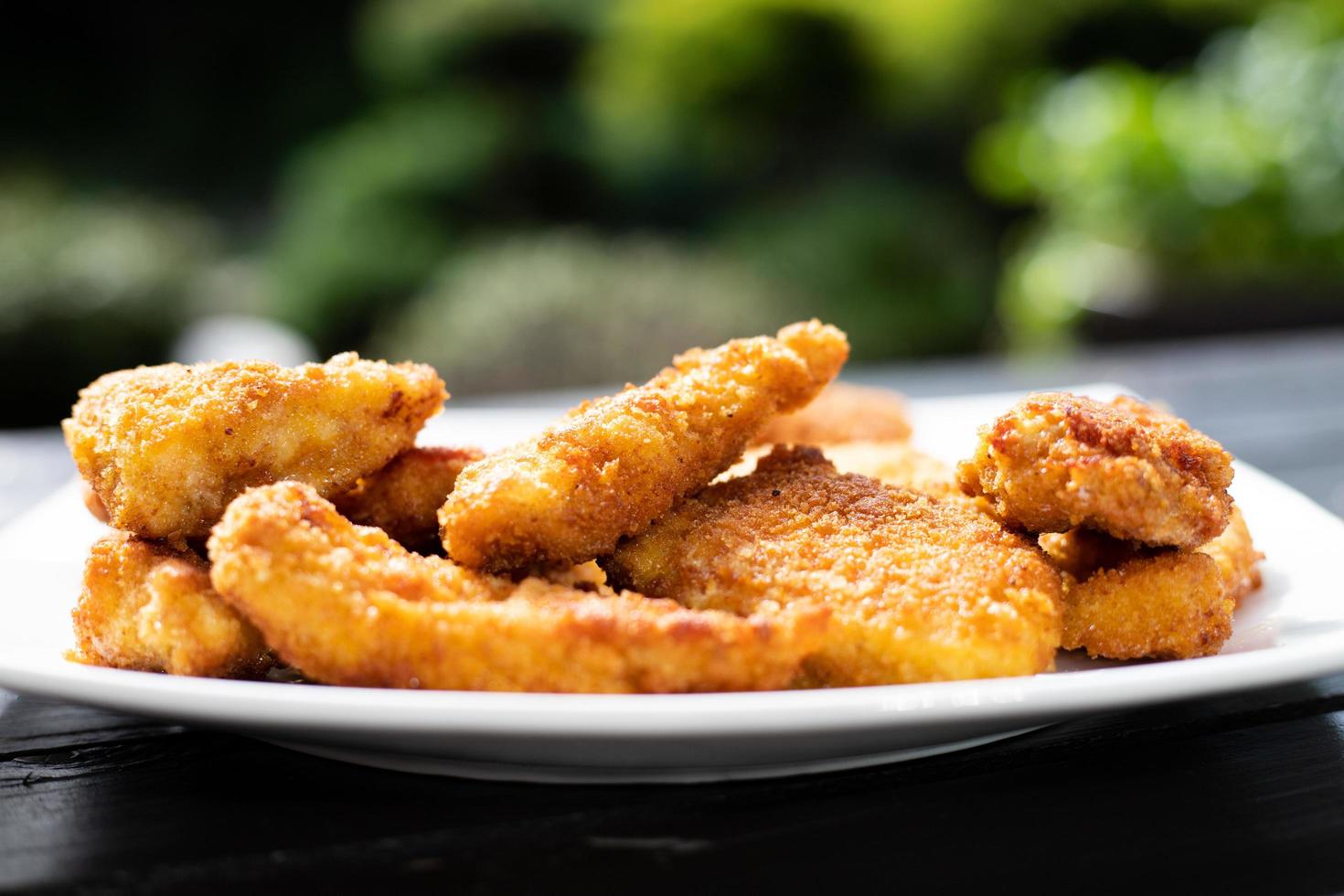 Breaded chicken pieces on a plate in a garden background. photo