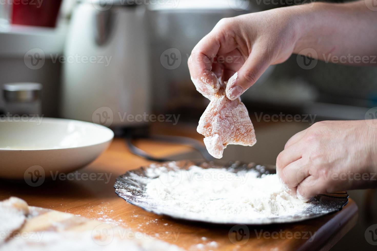 Breading chicken in flour. A person holding meat in his hand. photo