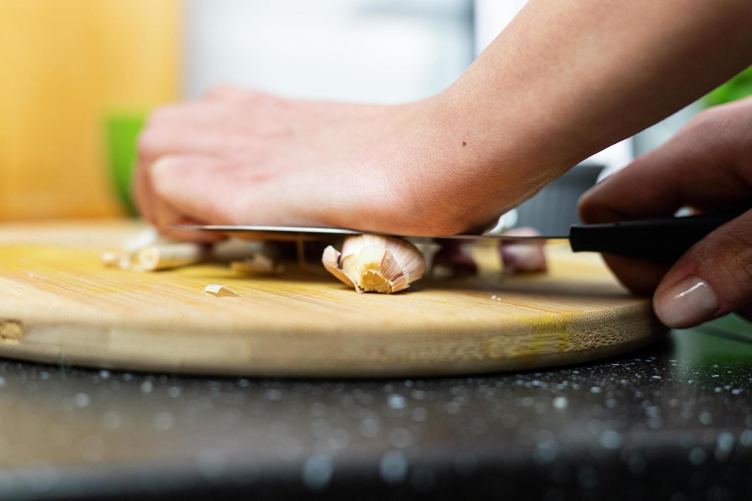A person crushing garlic with a knife. Preparation of the meal. photo