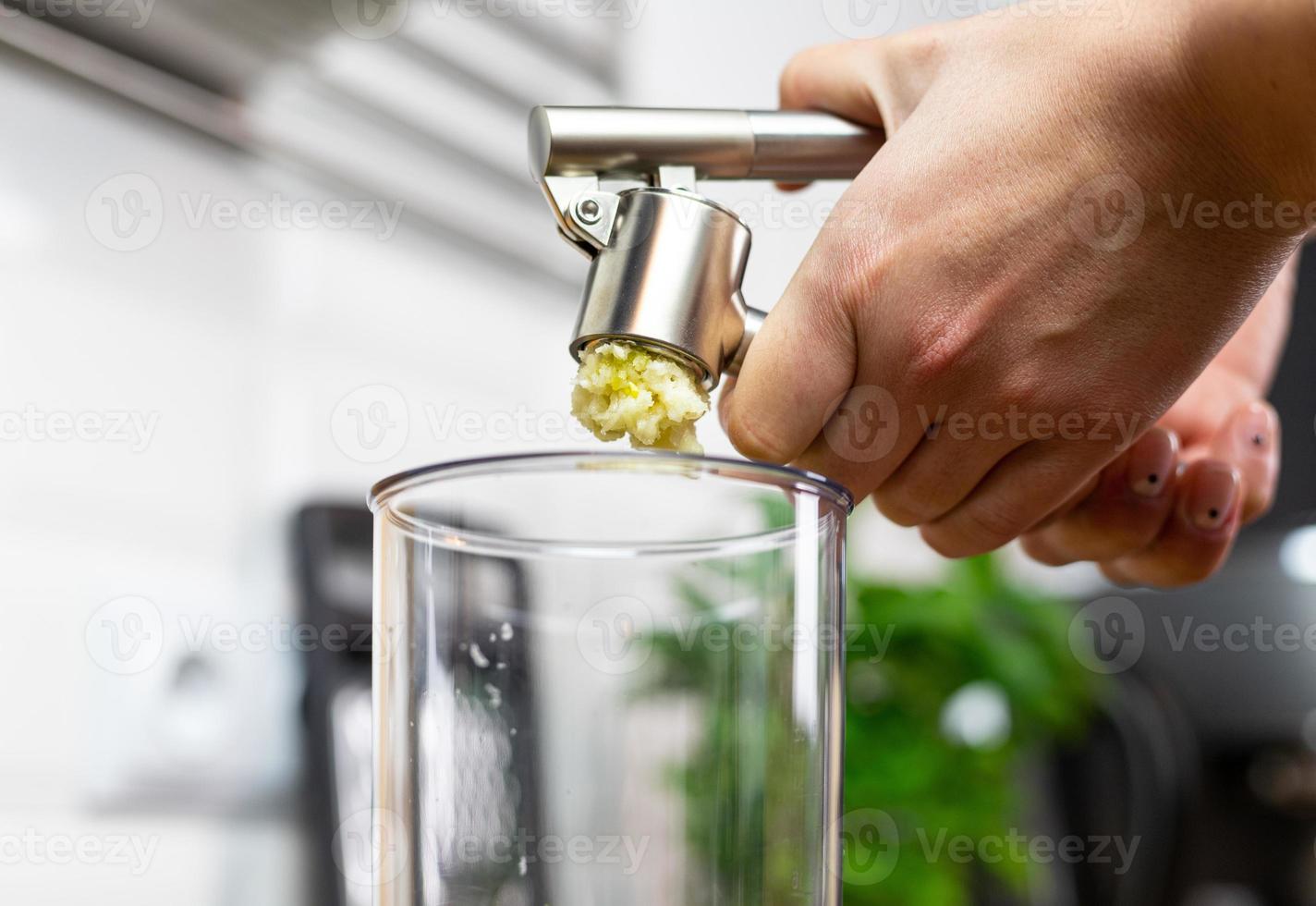 una persona exprimiendo ajo en un recipiente para licuar. preparación de pesto. foto