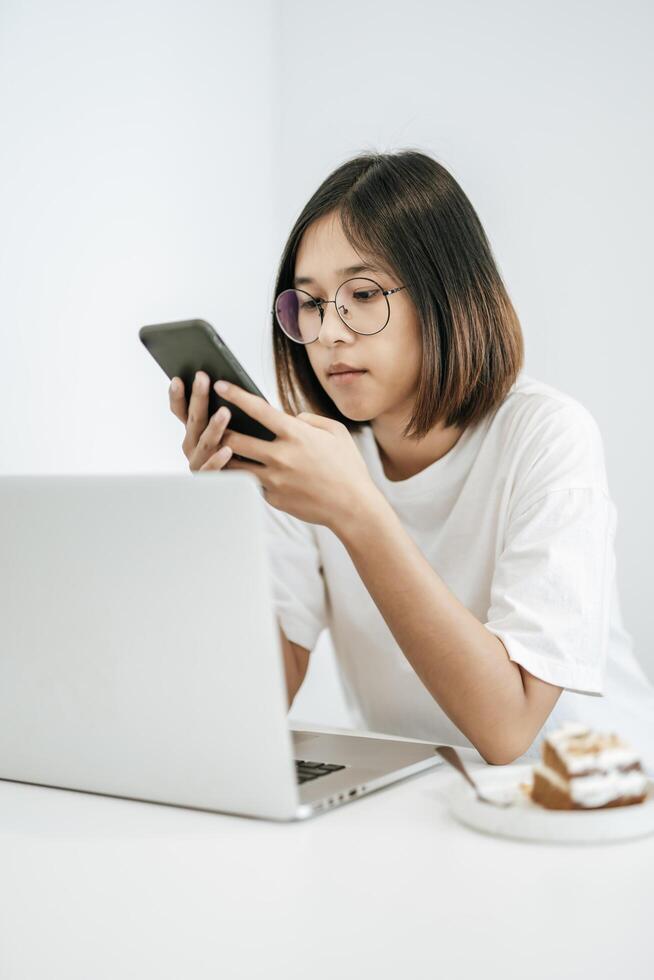 A woman wearing a white shirt, playing a smartphone and having a laptop. photo