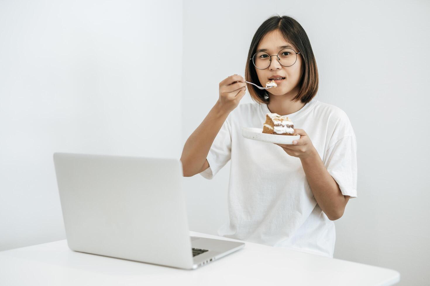 The girl eats cake and has a laptop on the table. photo