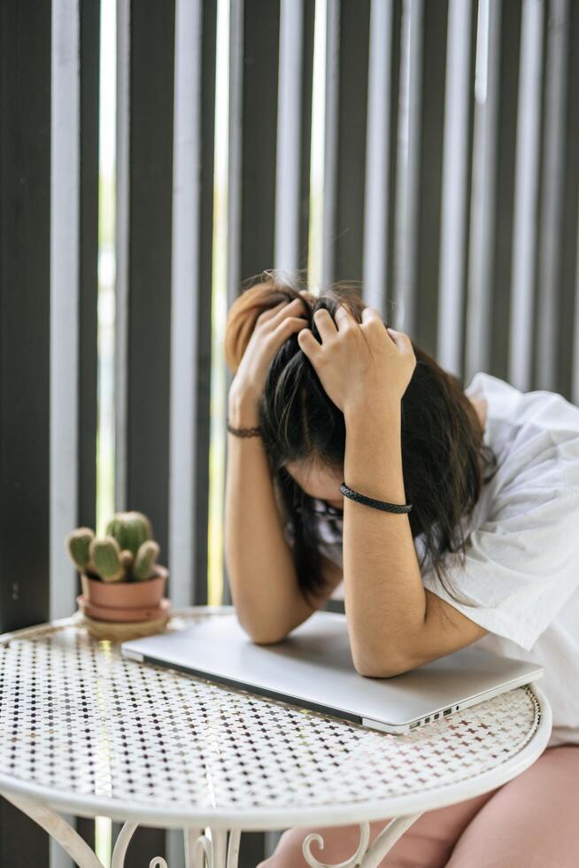 A woman wearing a mask playing a laptop and both hands holding the head photo