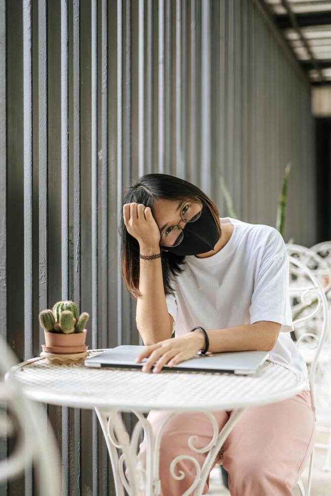 A woman wearing a mask playing a laptop and putting her head on her hand. photo