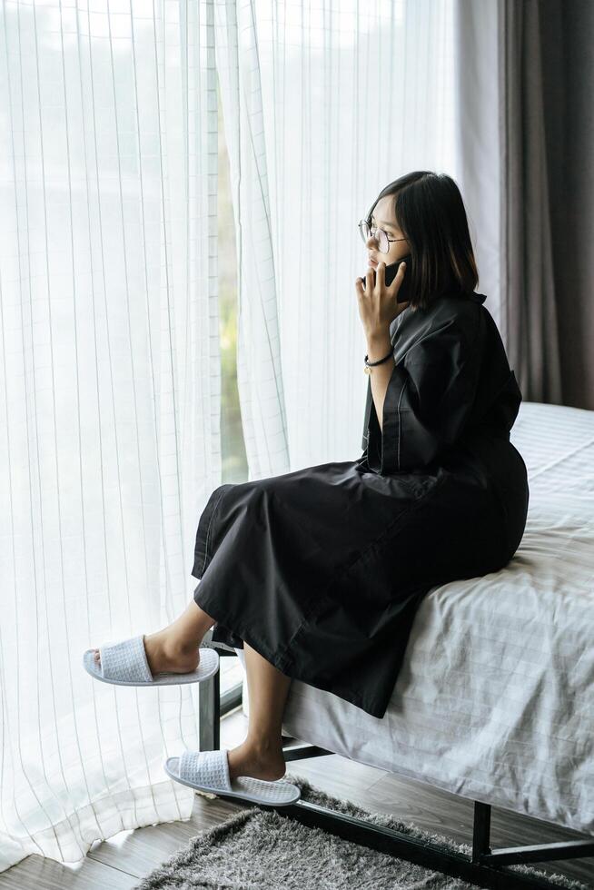 Woman wearing a white shirt, sitting on the bed and talking on the phone. photo