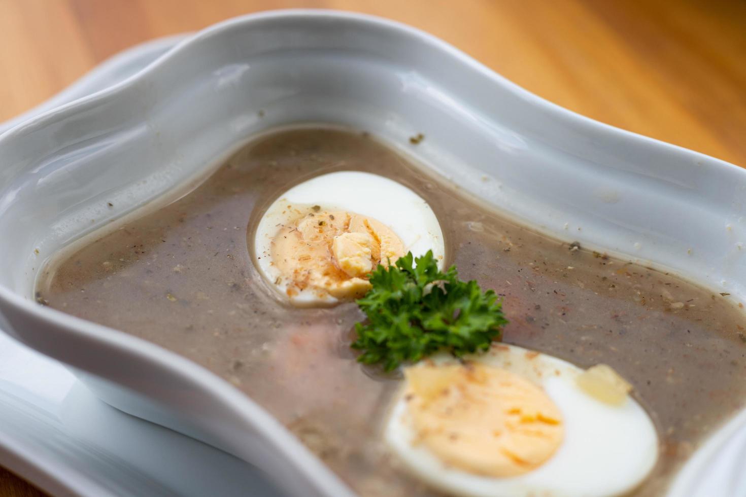 Pule la sopa de centeno agrio con huevo en un tazón blanco. foto