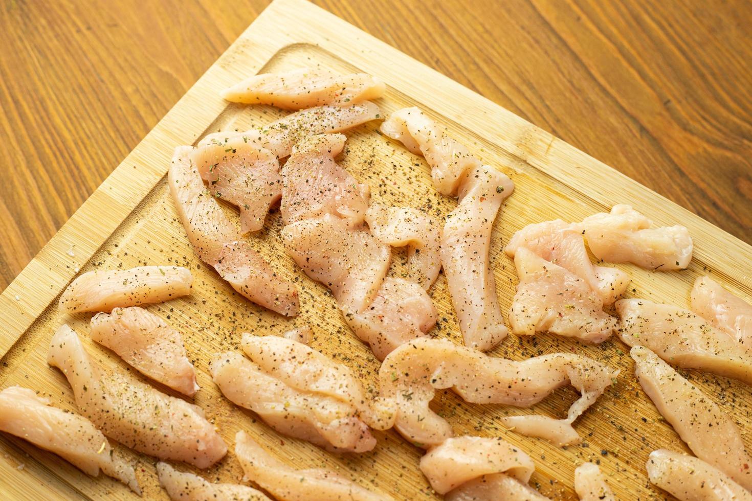 Piezas crudas de pollo sazonado con diversas especias acostado sobre una tabla de madera foto