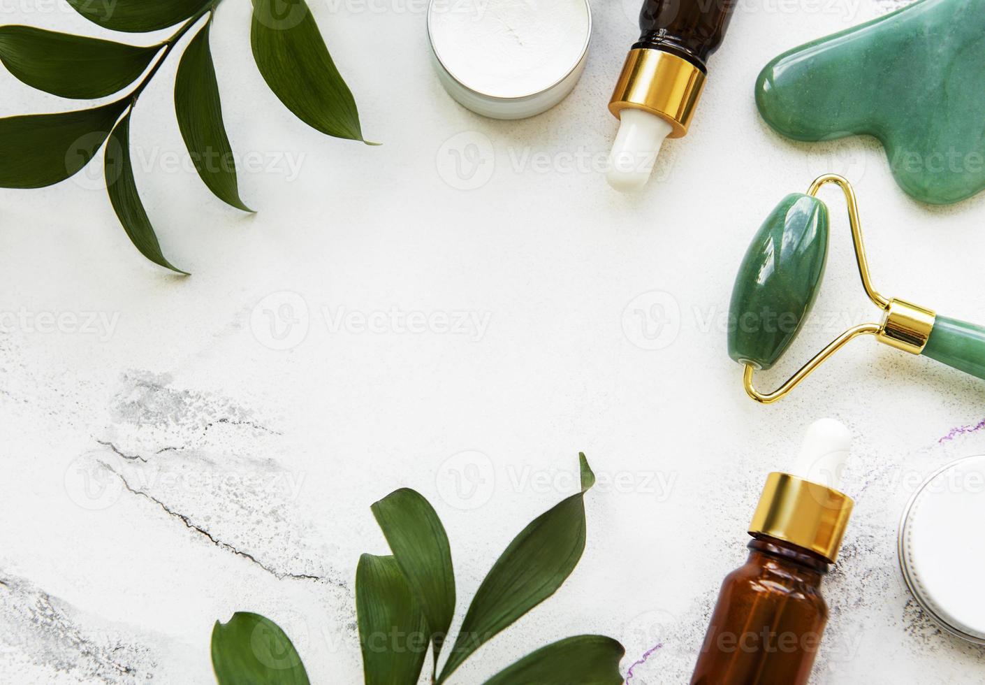 Rodillo de jade de masaje facial con producto cosmético sobre fondo de mármol blanco foto