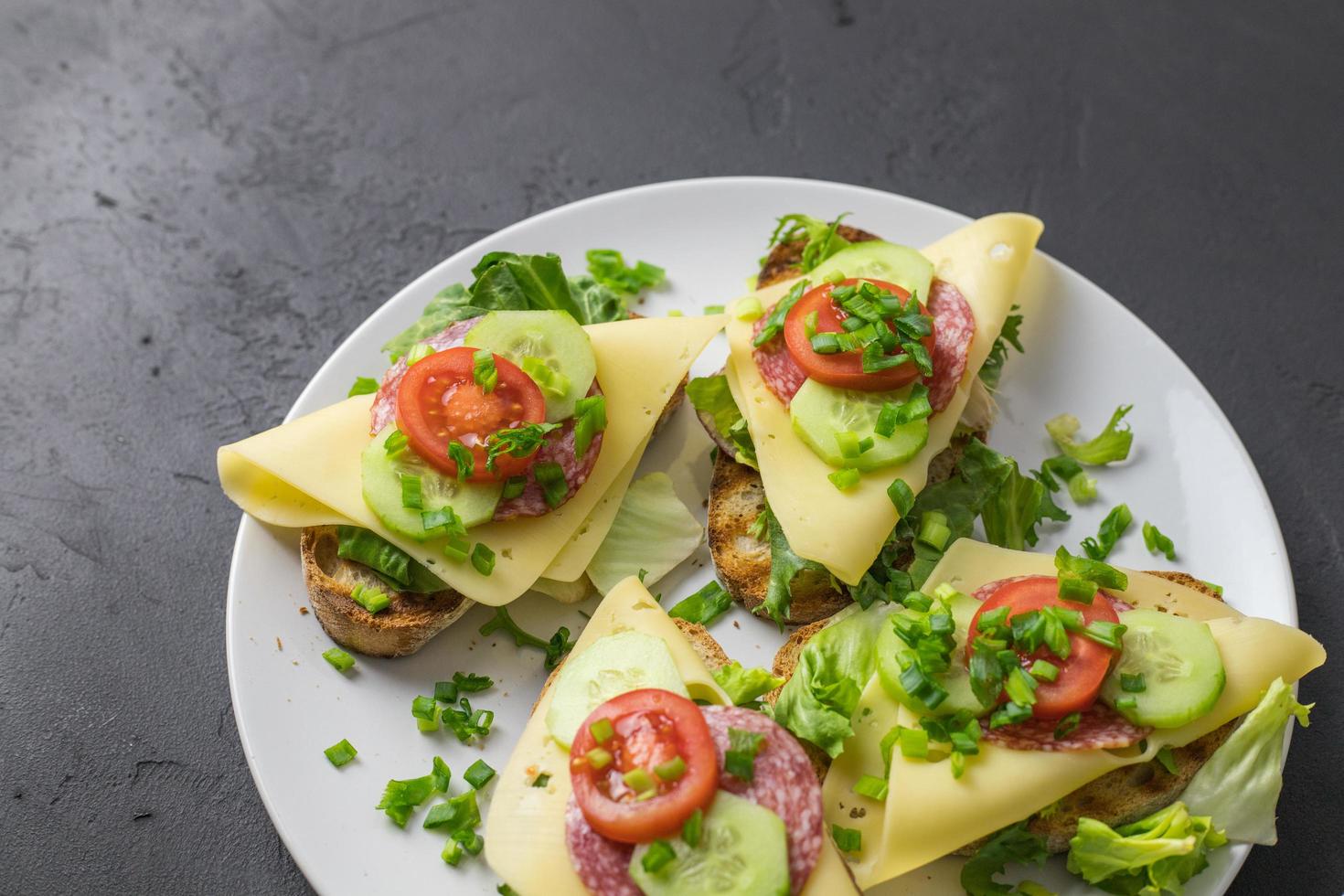 Sándwiches saludables de primavera con queso, lechuga y tomate espolvoreado con cebollino en platos acostado sobre un fondo oscuro foto