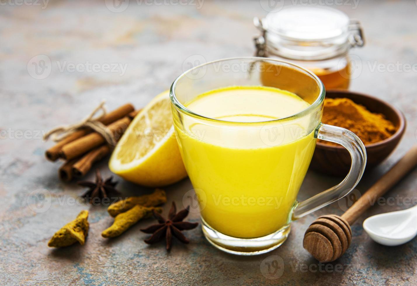 Yellow turmeric latte drink. Golden milk with cinnamon, turmeric, ginger  and honey over concrete background. photo