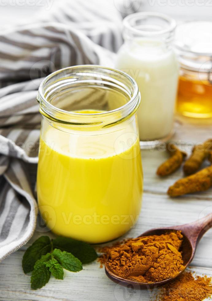 Yellow turmeric latte drink. Golden milk with cinnamon, turmeric, ginger  and honey over white wooden background. photo