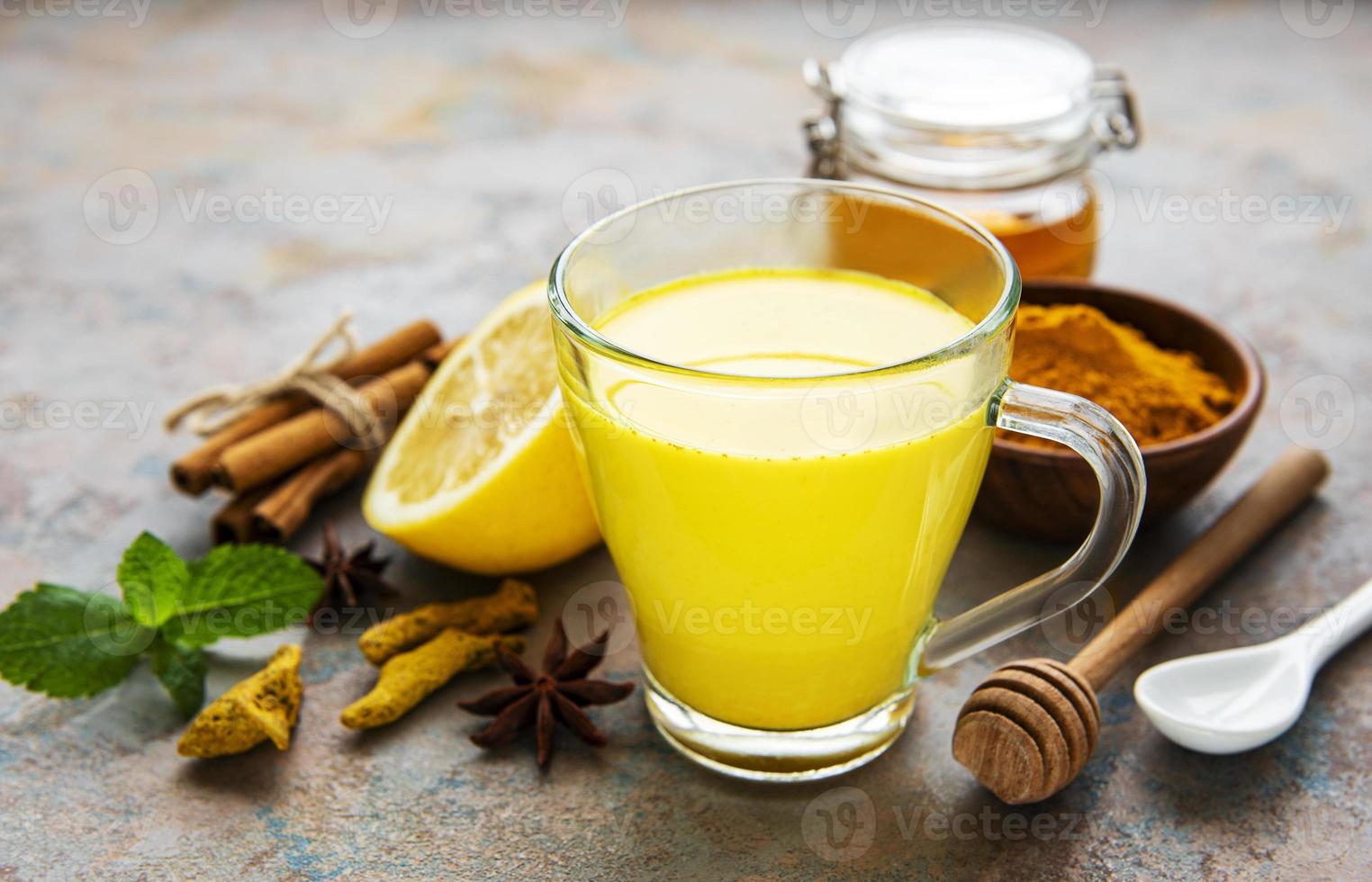 Yellow turmeric latte drink. Golden milk with cinnamon, turmeric, ginger  and honey over concrete background. photo