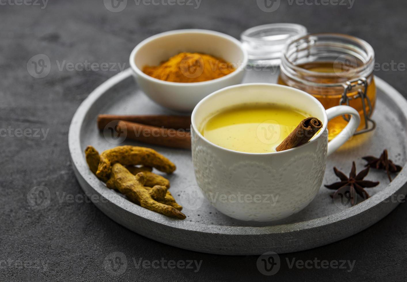Yellow turmeric latte drink. Golden milk with cinnamon, turmeric, ginger  and honey over black concrete background. photo