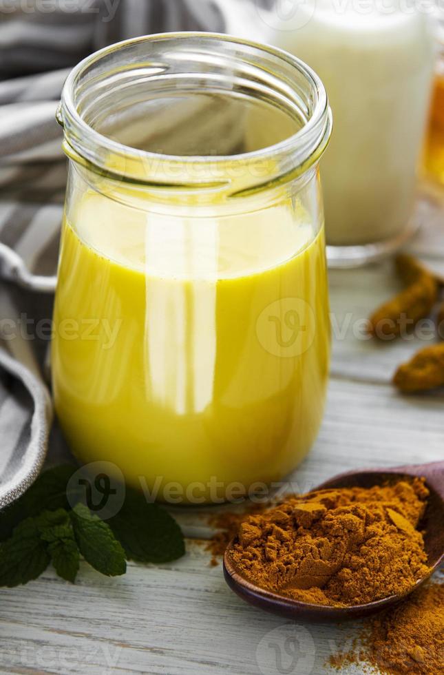 Yellow turmeric latte drink. Golden milk with cinnamon, turmeric, ginger  and honey over white wooden background. photo